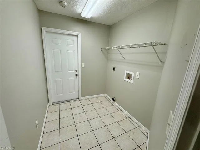 Clothes washing area featuring electric dryer hookup, light tile patterned floors, washer hookup, and a textured ceiling