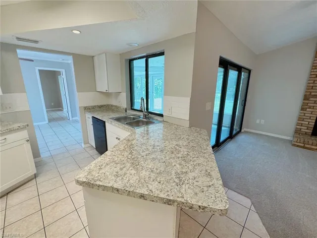 Kitchen featuring dishwasher, kitchen peninsula, lofted ceiling, light carpet, and white cabinets