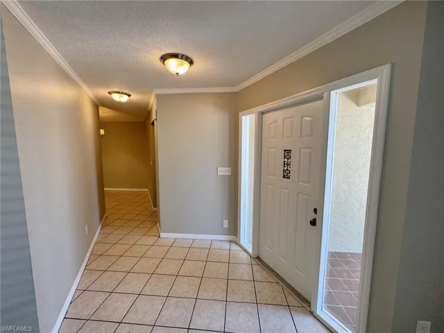 Entrance foyer featuring a textured ceiling, light tile patterned floors, and ornamental molding