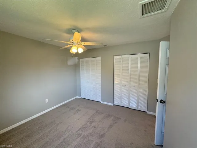 Guest bedroom 2 with light carpet, a textured ceiling, two closets, and ceiling fan