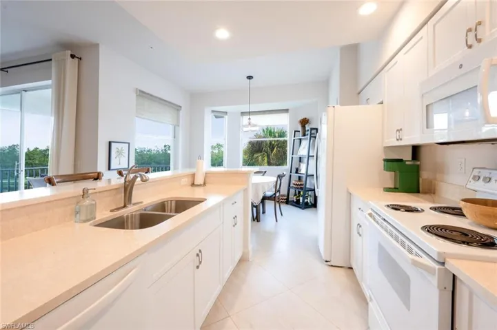 Kitchen featuring white appliances, white cabinets, recessed lighting, pendant lighting, and light stone counters