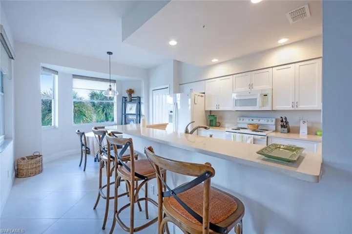 Kitchen with white cabinets, a breakfast bar area, white appliances, hanging light fixtures, and light stone countertops