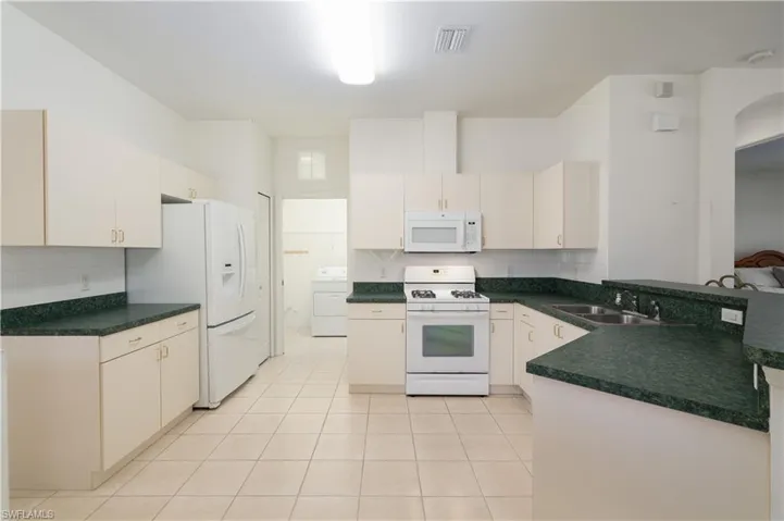 Kitchen with white appliances, washer / dryer, kitchen peninsula, sink, and light tile floors