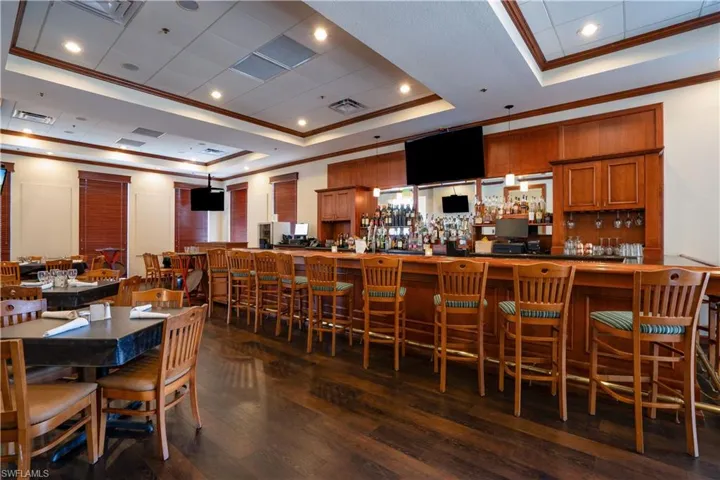 Dining room featuring dark hardwood / wood-style floors, a raised ceiling, ornamental molding, and indoor bar