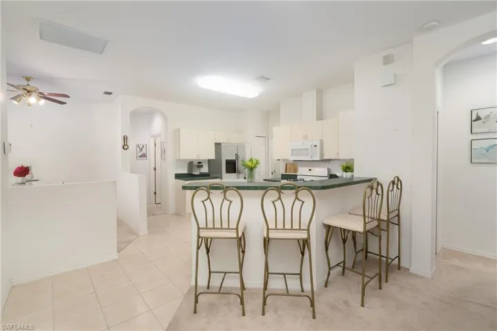 Kitchen featuring stainless steel fridge, white cabinets, kitchen peninsula, ceiling fan, and light tile floors