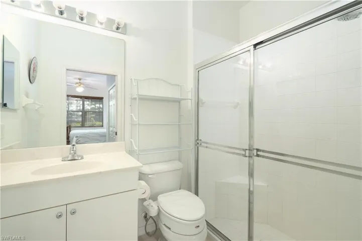 Bathroom with a shower with door, ceiling fan, toilet, and vanity