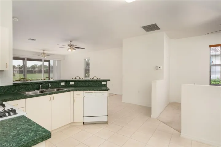 Kitchen featuring ceiling fan, light colored carpet, white dishwasher, sink, and white cabinetry
