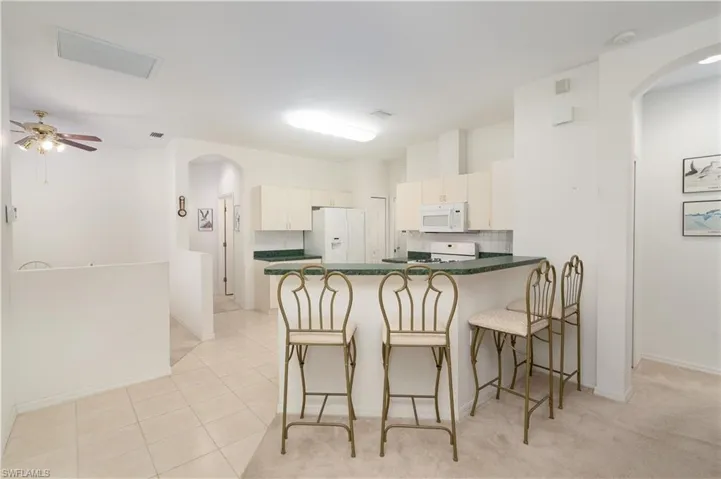 Kitchen with white cabinetry, white appliances, kitchen peninsula, light tile flooring, and ceiling fan