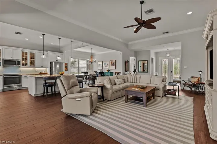 Living room featuring ornamental molding, dark wood-type flooring, ceiling fan with notable chandelier, and a healthy amount of sunlight