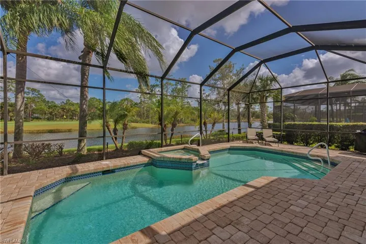 View of pool featuring a patio, an in ground hot tub, a water view, and glass enclosure