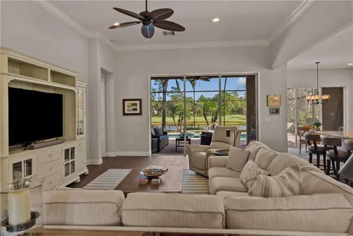 Living room with wood-type flooring, ornamental molding, and ceiling fan with notable chandelier