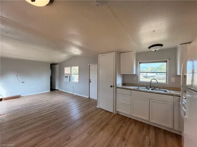 Kitchen with white cabinets, freestanding refrigerator, light wood-type flooring, open floor plan, and light countertops