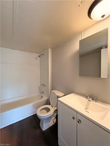 Bathroom with vanity, shower / bath combination, dark wood-style floors, and a textured ceiling