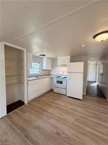 Kitchen with white appliances, white cabinets, light wood-style floors, light countertops, and a textured ceiling