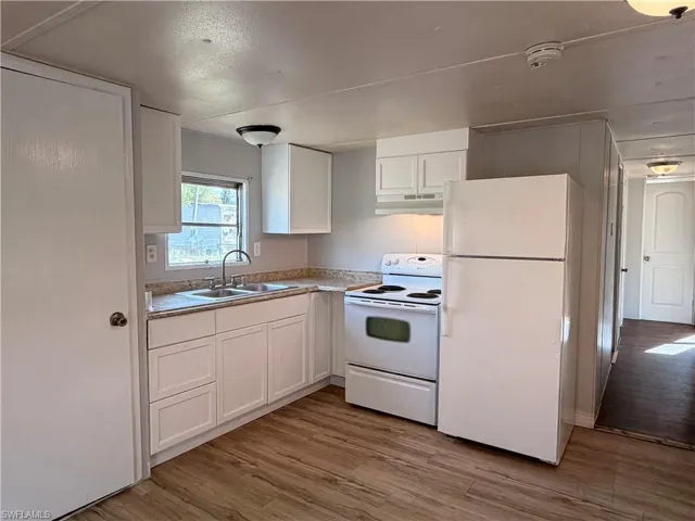 Kitchen with white appliances, white cabinetry, light wood-style flooring, and light countertops