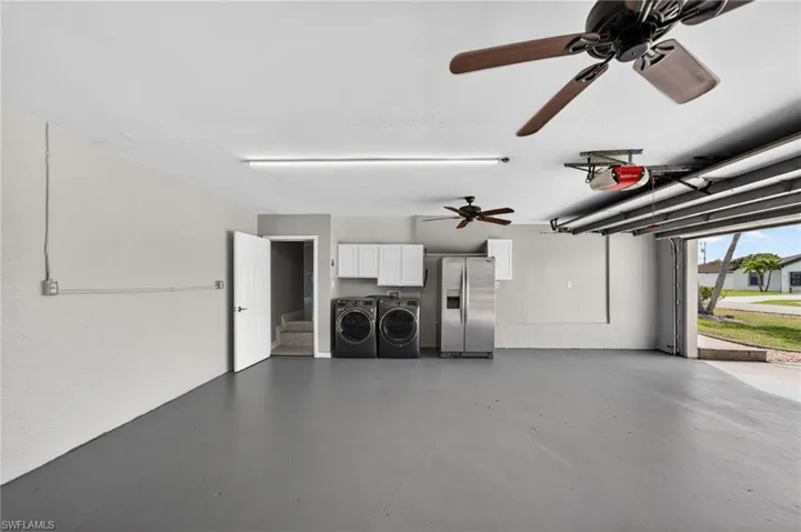 Garage featuring stainless steel refrigerator with ice dispenser, ceiling fan, washing machine and clothes dryer, and a garage door opener