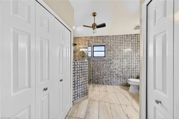 Full bathroom featuring a closet, a walk in shower, ceiling fan, and tile walls