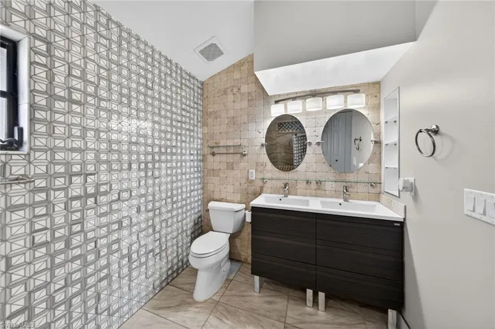 Bathroom with tile walls, double vanity, and lofted ceiling