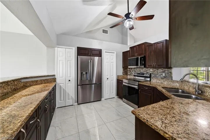 Kitchen with stainless steel appliances, dark wood finish cabinetry, light stone countertops, ceiling fan, and light marble finish floors