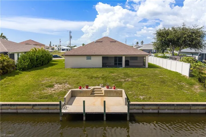Waterfront property featuring a private boat dock, concrete seawall, expansive grassy backyard, screened patio, and a shingle roof