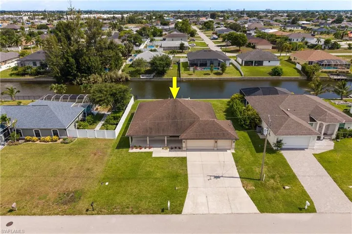 Canal-front property featuring a two-car garage, mature landscaping, and a concrete driveway