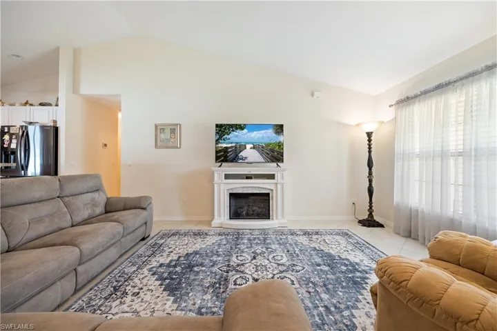 Vaulted ceiling living area featuring light-toned tile flooring and an electric fireplace with a white mantel
