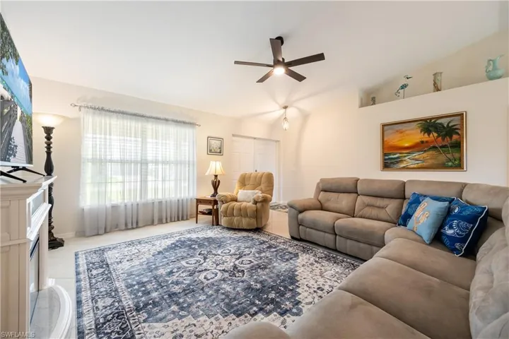 Living area featuring vaulted ceilings, a ceiling fan, tiled flooring, and a large window with sheer curtains