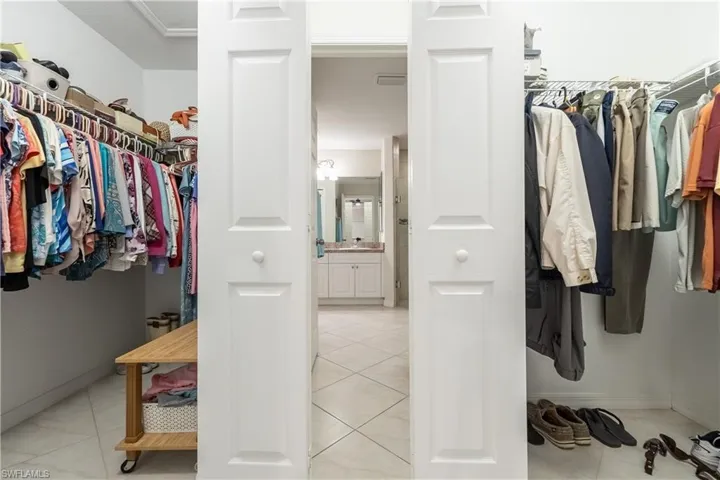 Walk-through closet featuring white wire shelving, white bi-fold doors, and neutral tile flooring