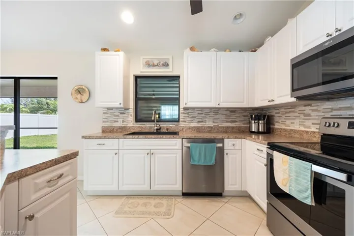 Kitchen featuring white cabinetry, light-toned countertops, a mosaic tile backsplash, and stainless steel appliances