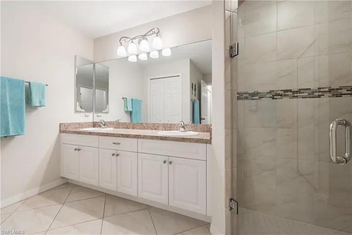 Bathroom featuring a dual vanity with white cabinetry, a large mirror, and a glass-enclosed shower with tiled walls and an accent mosaic band