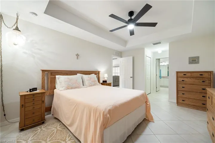 Spacious bedroom featuring a tray ceiling, ceiling fan, and light-toned tile flooring