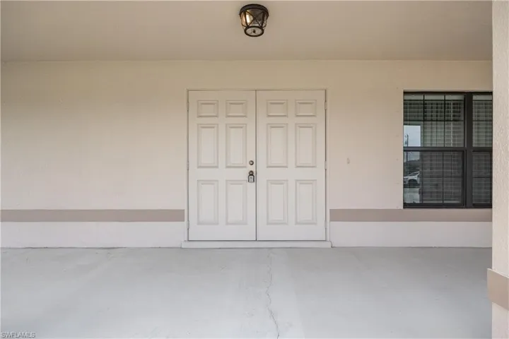 Recessed entry with double panel doors, an overhead enclosed light fixture, and an adjacent window with dark trim