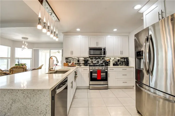 Kitchen featuring appliances with stainless steel finishes, a peninsula, white cabinetry, light stone countertops, and pendant lighting