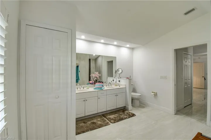 Bathroom featuring a closet, double vanity, vaulted ceiling, and recessed lighting