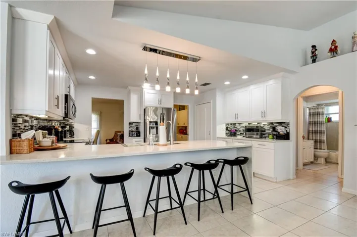 Kitchen with arched walkways, tasteful backsplash, a breakfast bar, white cabinetry, and a peninsula