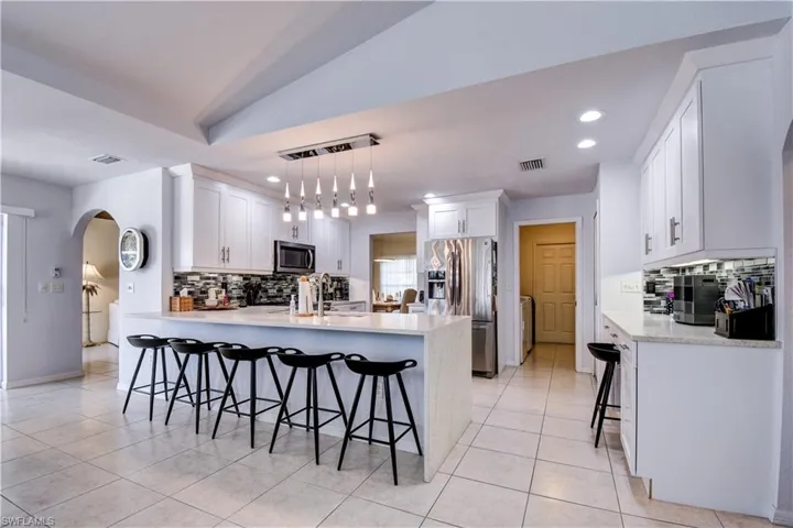 Kitchen featuring a breakfast bar, arched walkways, a peninsula, appliances with stainless steel finishes, and white cabinets