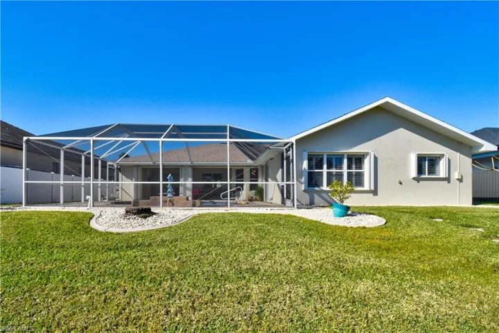 Back of house with a lanai, a sunroom, stucco siding, and a lawn