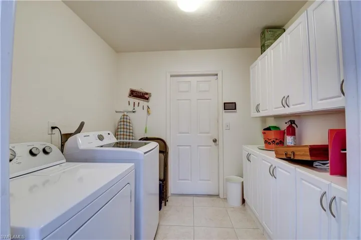 Laundry room with cabinet space, washing machine and dryer, light tile patterned floors, and a textured ceiling