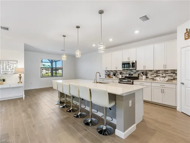 Kitchen with appliances with stainless steel finishes, sink, an island with sink, white cabinetry, and pendant lighting