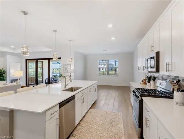 Kitchen featuring an island with sink, light hardwood / wood-style flooring, stainless steel appliances, sink, and decorative light fixtures
