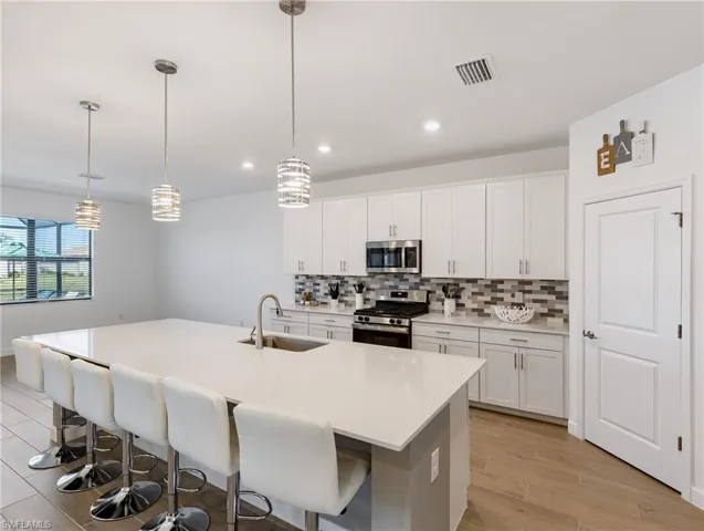 Kitchen with appliances with stainless steel finishes, white cabinetry, a kitchen island with sink, sink, and decorative light fixtures