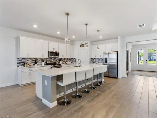 Kitchen with appliances with stainless steel finishes, white cabinetry, a kitchen island with sink, pendant lighting, and sink