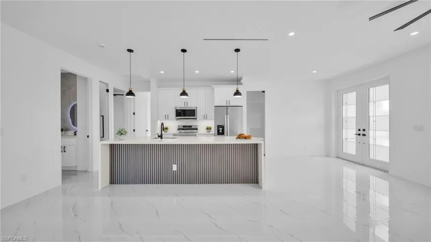 Kitchen with white cabinetry, appliances with stainless steel finishes, french doors, light stone counters, and a large island
