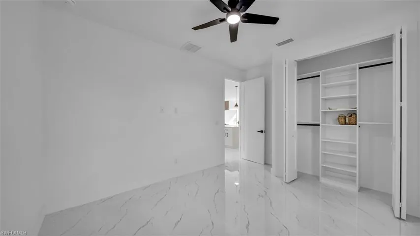 Unfurnished bedroom featuring light marble finish flooring, ceiling fan, and a closet