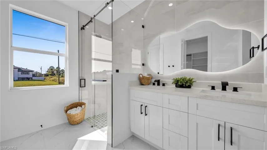 Bathroom featuring a shower stall, double vanity, and light marble finish floors