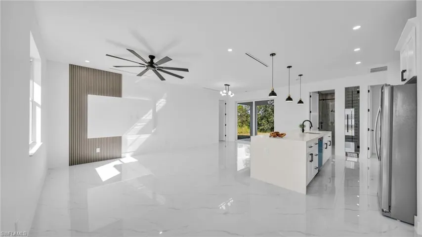 Kitchen featuring light marble finish floors, a kitchen island with sink, open floor plan, pendant lighting, and freestanding refrigerator