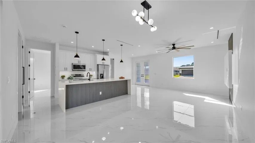 Kitchen with white cabinetry, open floor plan, light marble finish floors, a large island with sink, and hanging light fixtures