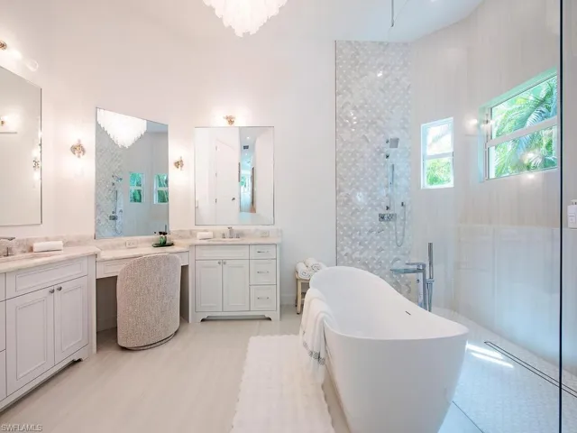 Spacious bathroom featuring a free-standing soaking tub, a walk-in shower with patterned tile, double vanities with stone countertops, and recessed lighting