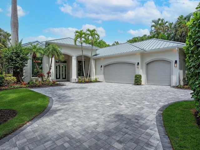 Contemporary stucco exterior featuring a metal roof, arched garage doors, and a paver driveway