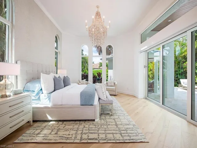 Spacious bedroom featuring light wood-finish flooring, a crystal chandelier, arched windows, and sliding glass doors opening to a paved patio